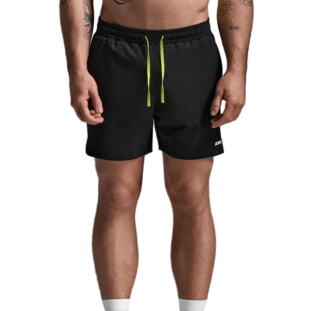 A man wearing black athletic shorts with a bright lime green drawstring, paired with white socks and white sneakers, shown from the waist down against a gray studio background.