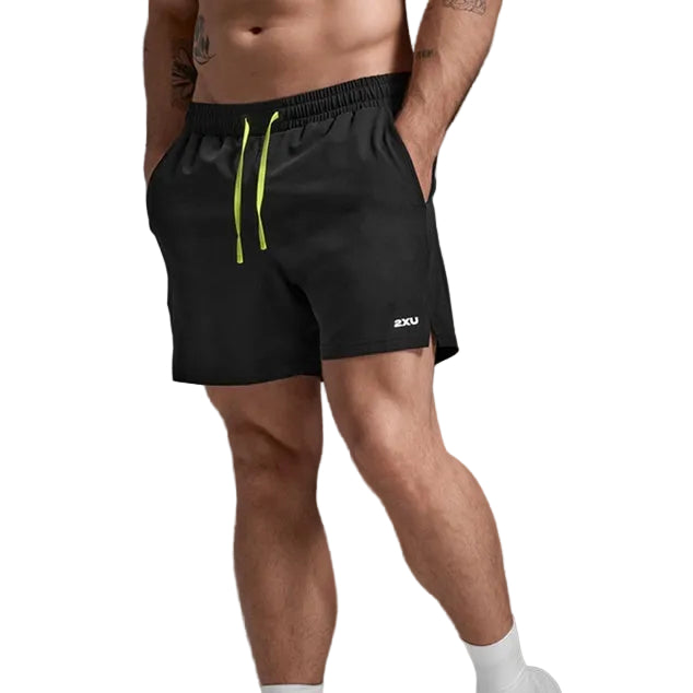 A man wearing black athletic shorts with a bright neon yellow-green drawstring and a small white logo on the lower left leg, paired with white socks and white sneakers, against a dark gray studio background.
