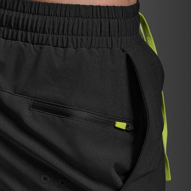 Close-up of black athletic shorts with a side zip pocket, elastic waistband, and a bright neon yellow-green drawstring visible on the right side.