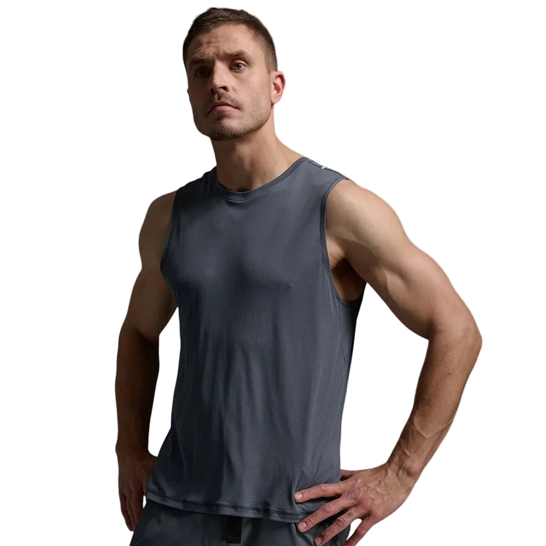 A muscular man wearing a dark gray sleeveless athletic tank top and matching gray athletic pants, posing against a light gray studio background.