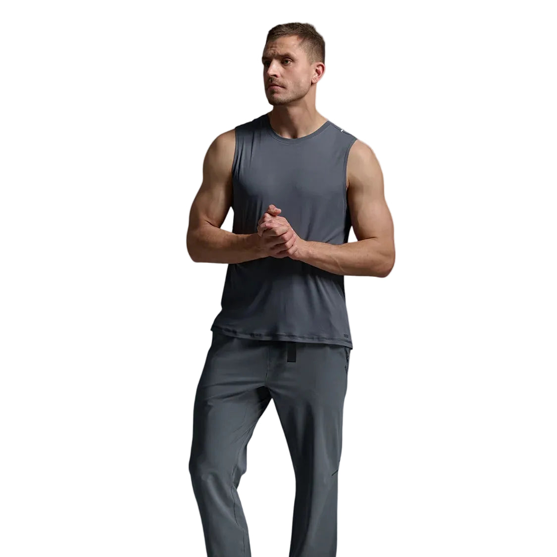 A man modeling a dark gray sleeveless athletic tank top and matching gray jogger pants, paired with olive green sneakers, against a light gray studio background.