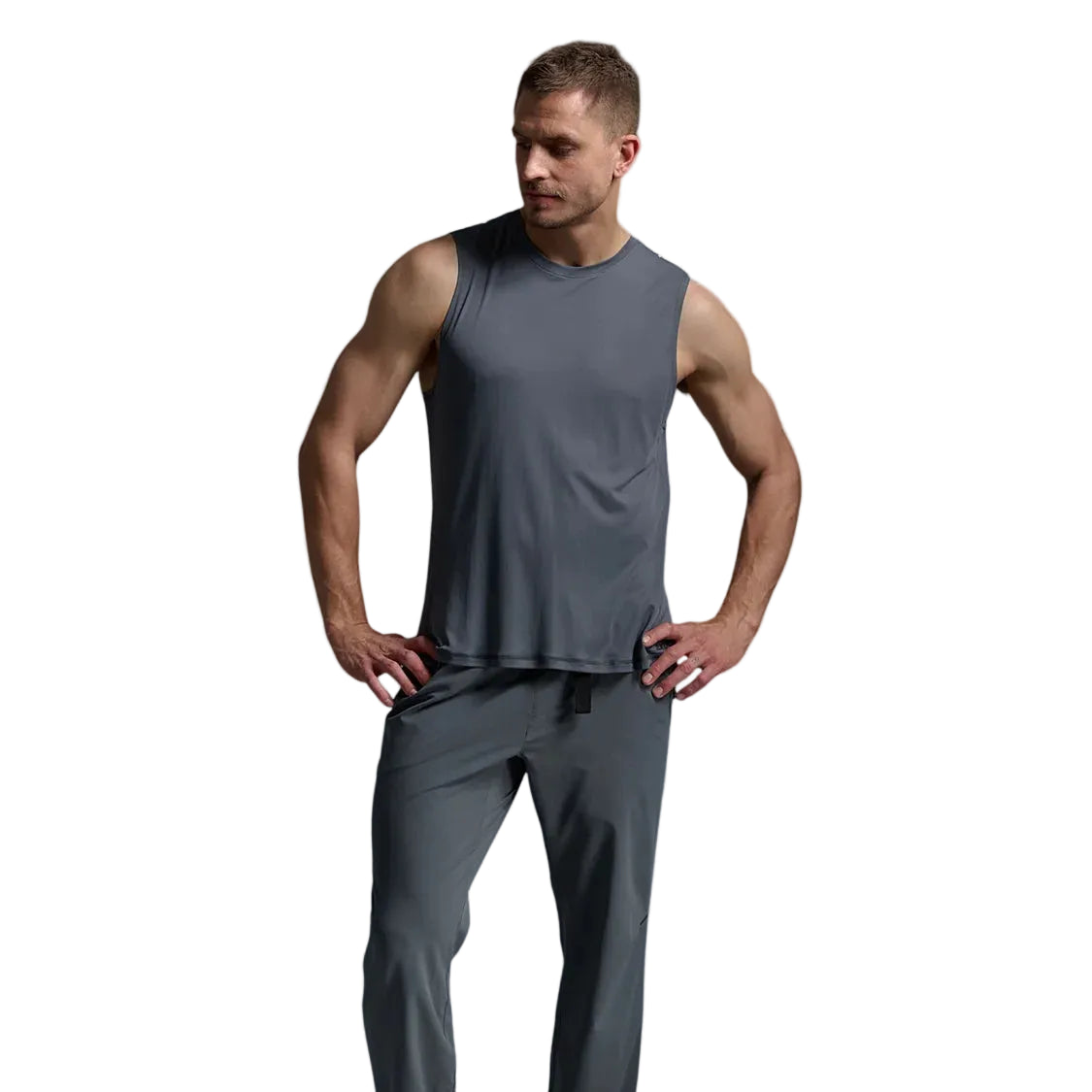 A man modeling a dark gray sleeveless athletic tank top and matching gray jogger pants, standing against a light gray studio background.