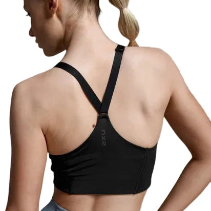 A woman shown from the back wearing a black sports bra with crossover straps and a visible 2XU logo, paired with light blue leggings, against a neutral gray studio background.