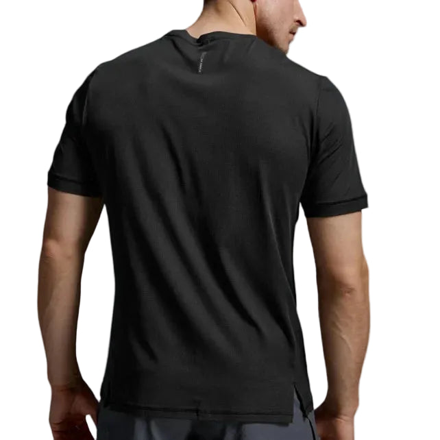 A man viewed from behind wearing a black short-sleeve athletic t-shirt and gray shorts against a light gray studio background.