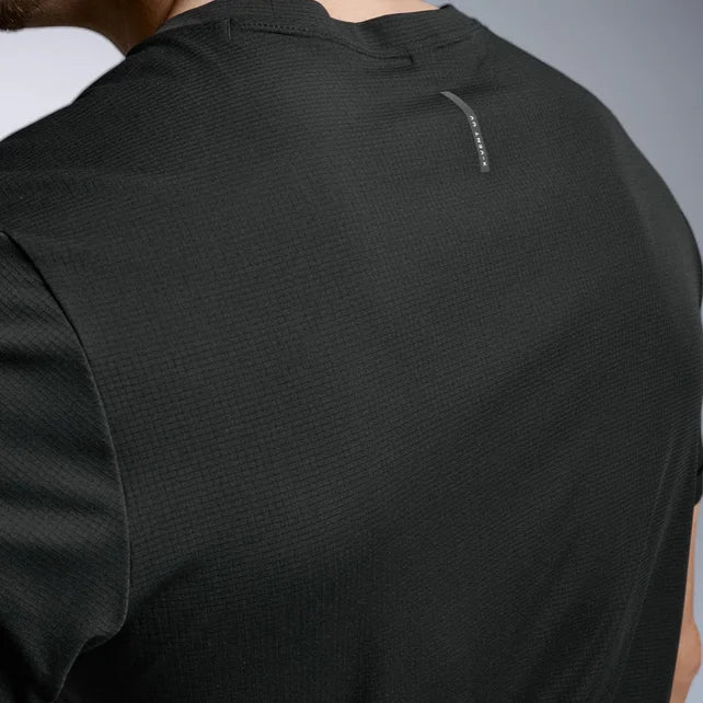 Close-up back view of a person wearing a black textured athletic short-sleeve shirt with a small vertical logo near the upper neckline, against a light gray studio background.