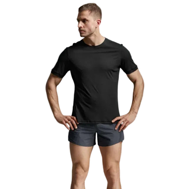 A man modeling a black short-sleeve athletic t-shirt and dark gray running shorts, paired with off-white socks and running shoes, against a light gray studio background.
