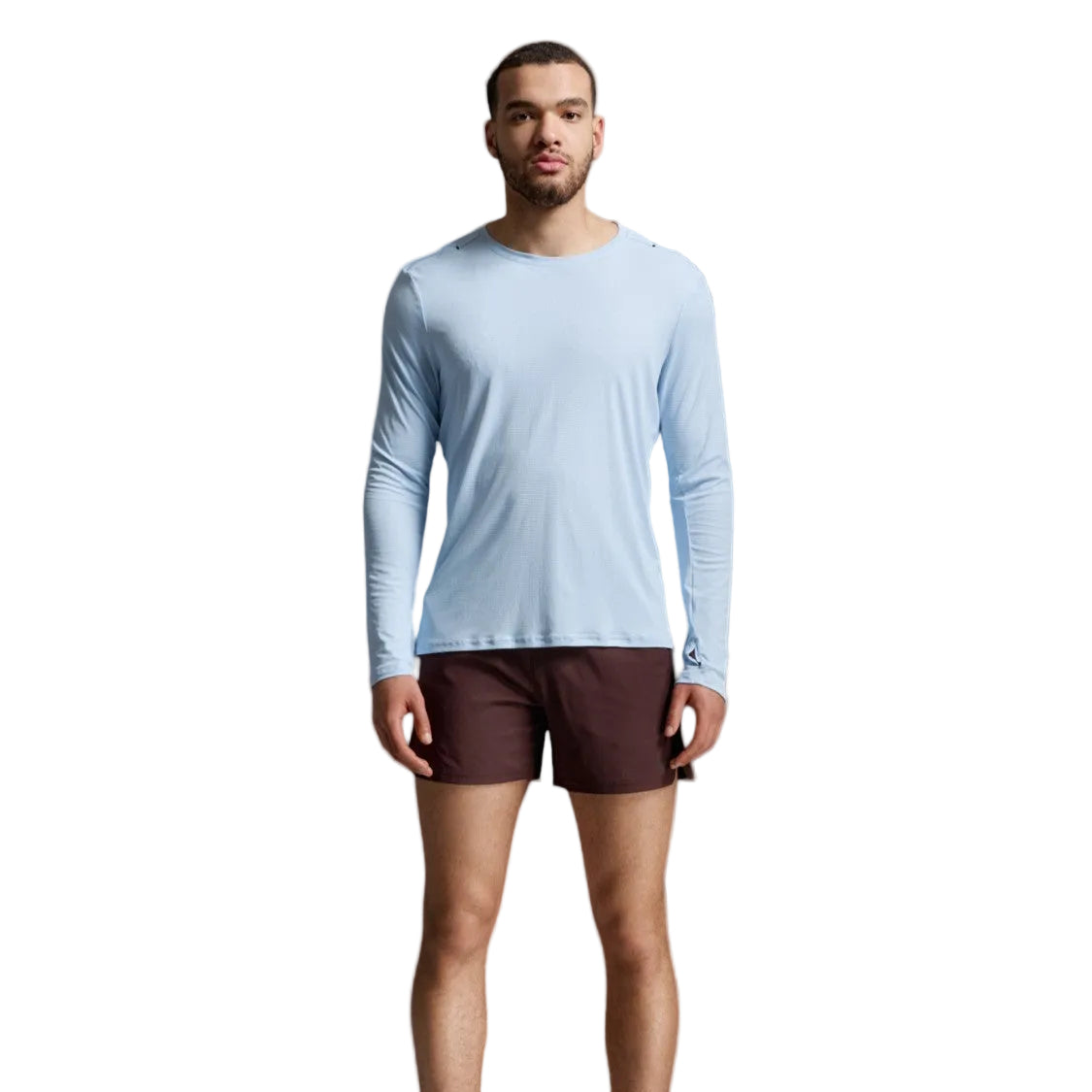 A man modeling a light blue long-sleeve athletic shirt and dark brown shorts against a light gray studio background.