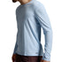 A man wearing a light blue long-sleeve athletic shirt and dark brown shorts, shown from a side profile against a neutral gray studio background.