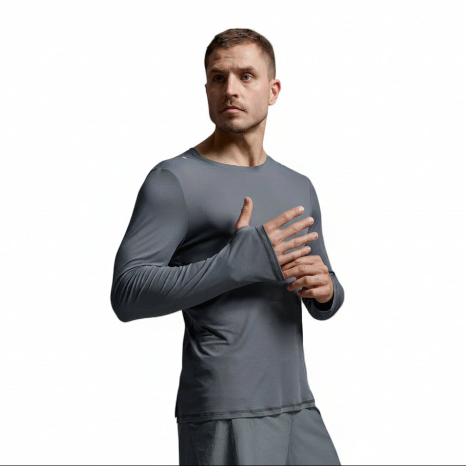 A man wearing a tight-fitting long-sleeve athletic shirt in dark gray, posed against a neutral light gray studio background.