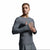 A man wearing a tight-fitting long-sleeve athletic shirt in dark gray, posed against a neutral light gray studio background.