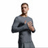 A man wearing a tight-fitting long-sleeve athletic shirt in dark gray, posed against a neutral light gray studio background.