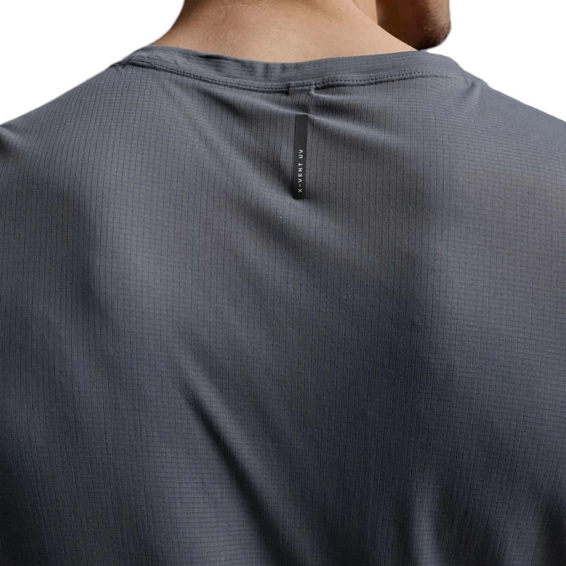 Close-up back view of a person wearing a dark gray textured athletic t-shirt, showing the neck collar and a small vertical black brand tag.
