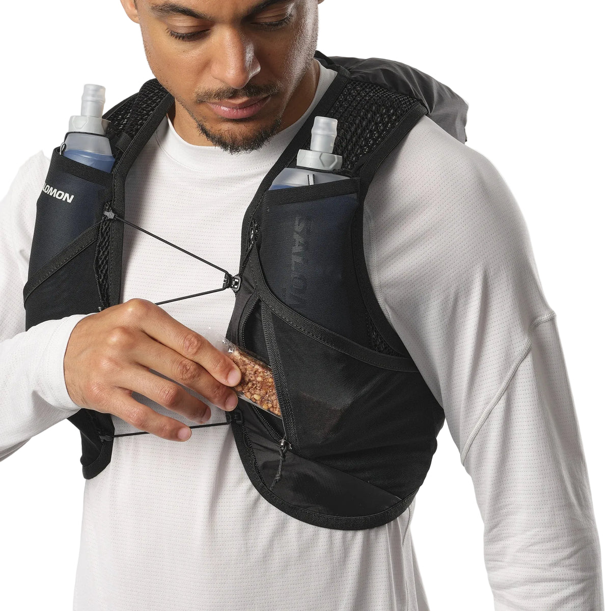 Person wearing a black hydration vest with water bottles and snacks.