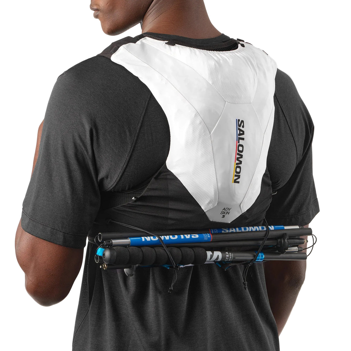 Person wearing a Salomon hydration pack with hiking poles on a plain background