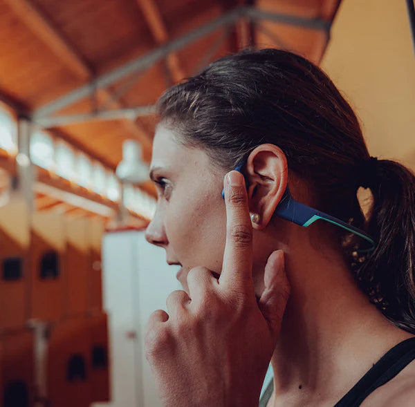 Person adjusting a blue wireless earbud in an indoor setting