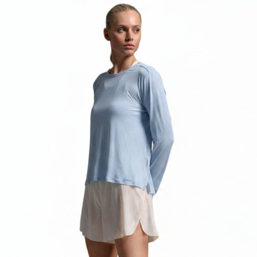 A woman modeling a light blue long-sleeve athletic top and a light beige skirt, standing against a light gray studio background.