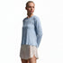 A woman modeling a light blue long-sleeve athletic top and a light beige skirt, standing against a light gray studio background.