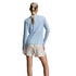 A woman shown from behind wearing a light blue long-sleeve athletic top, beige running shorts, light blue socks, and gray running shoes against a light gray studio background.
