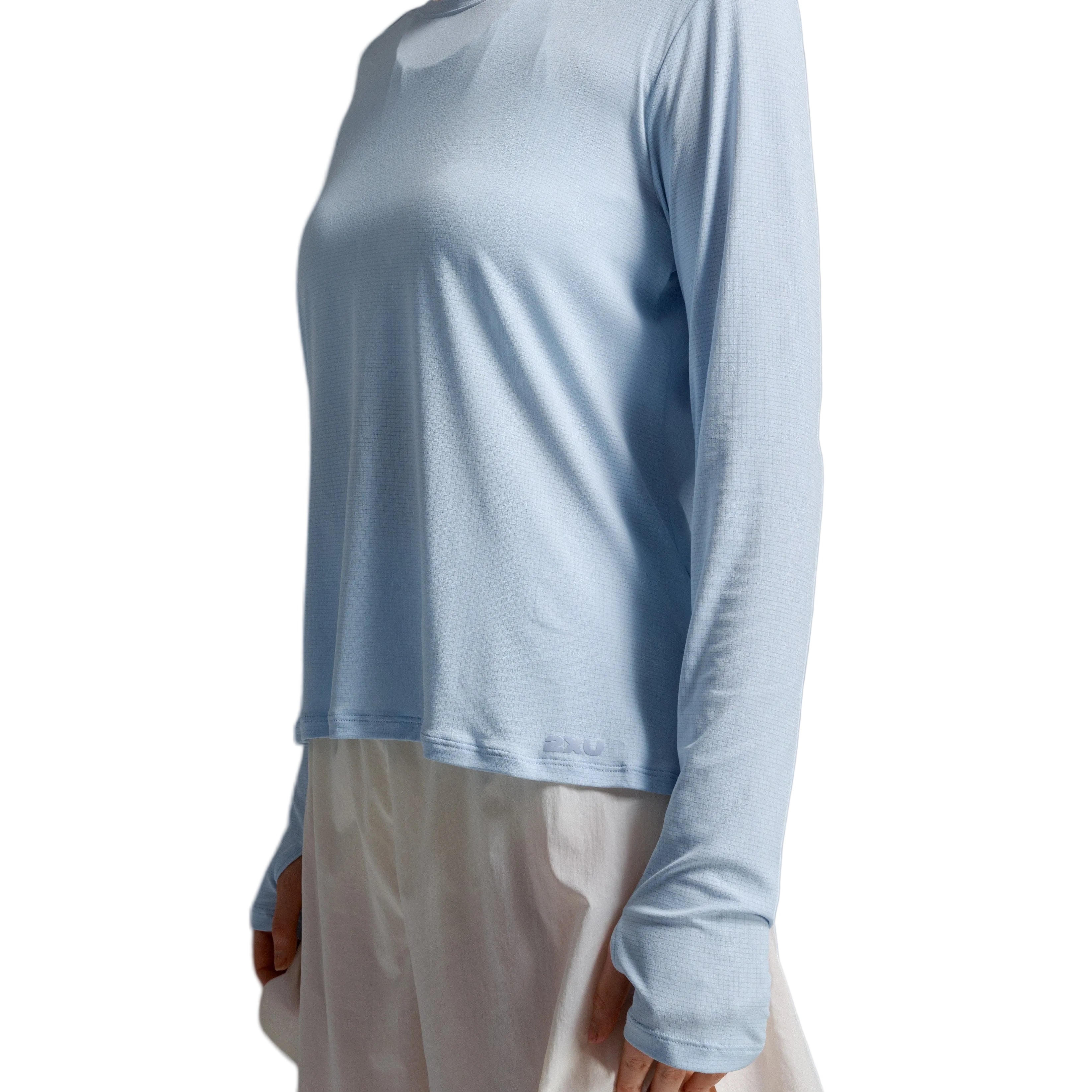 A model wearing a light blue long-sleeve crewneck top layered over a cream-colored dress, shown from the neck down against a neutral gray studio background.