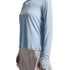 A model wearing a light blue long-sleeve crewneck top layered over a cream-colored dress, shown from the neck down against a neutral gray studio background.