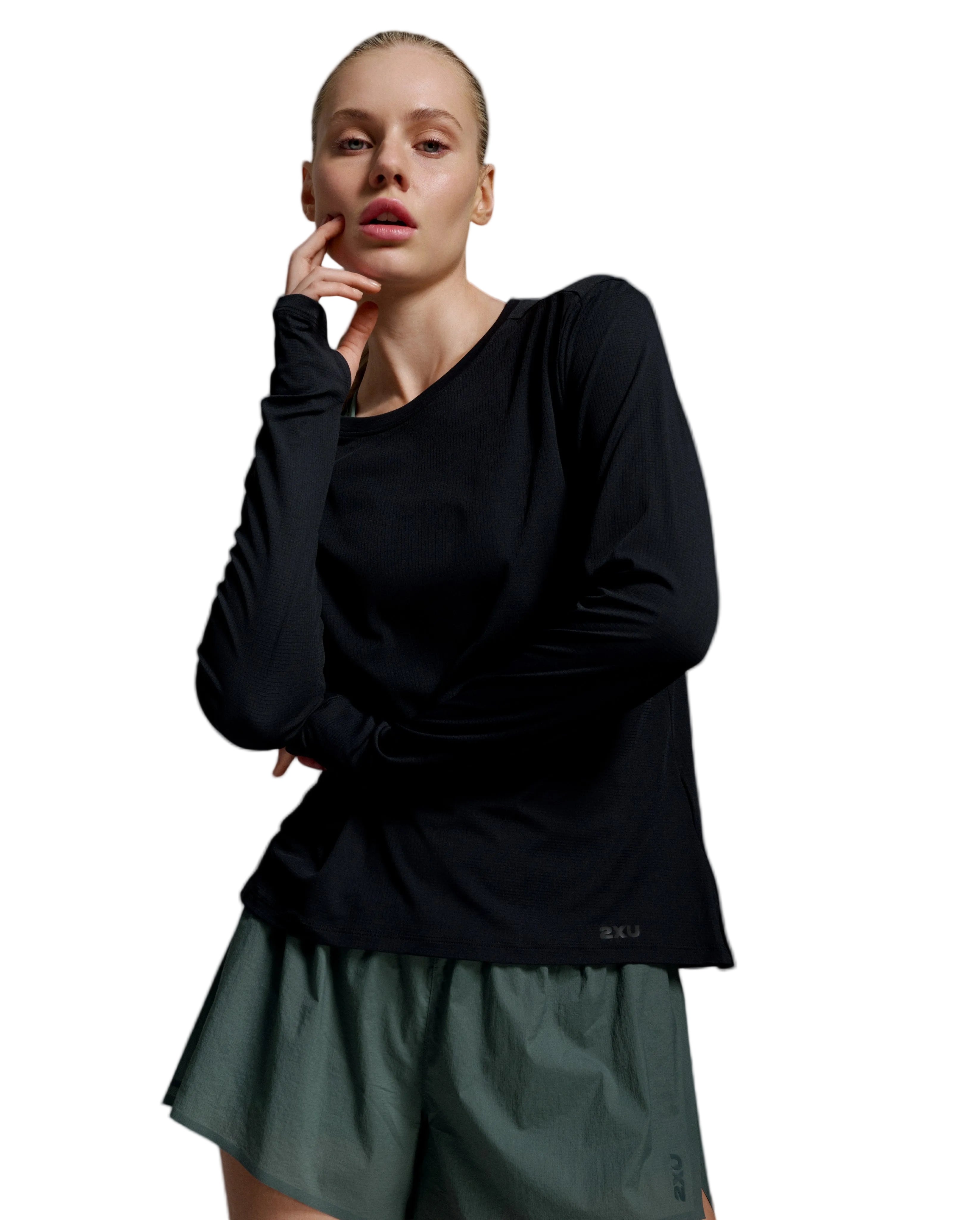 A woman modeling a black long-sleeve athletic top and olive green shorts against a light gray studio background.