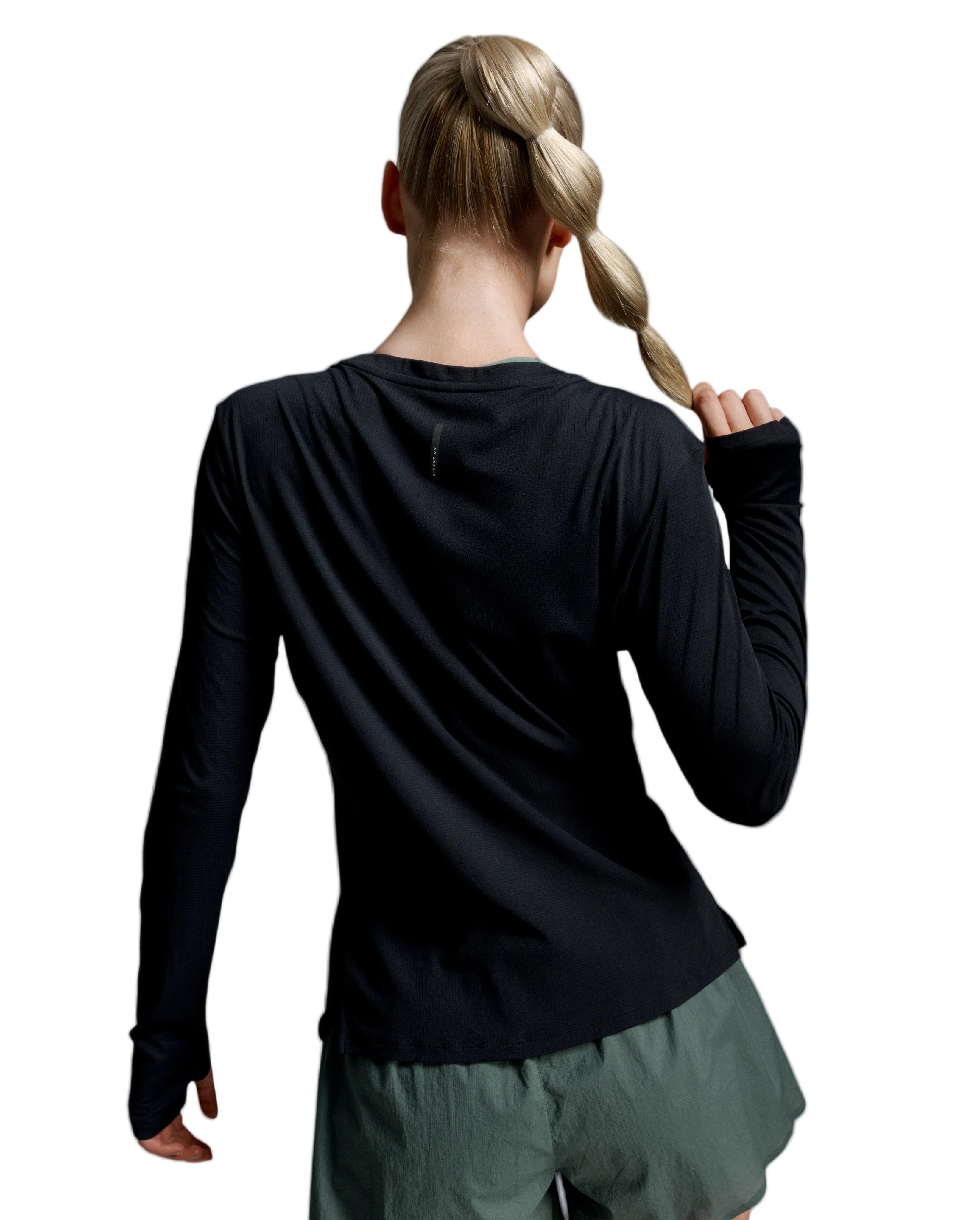 A woman shown from behind wearing a black long-sleeve athletic top and olive green shorts against a light gray studio background.