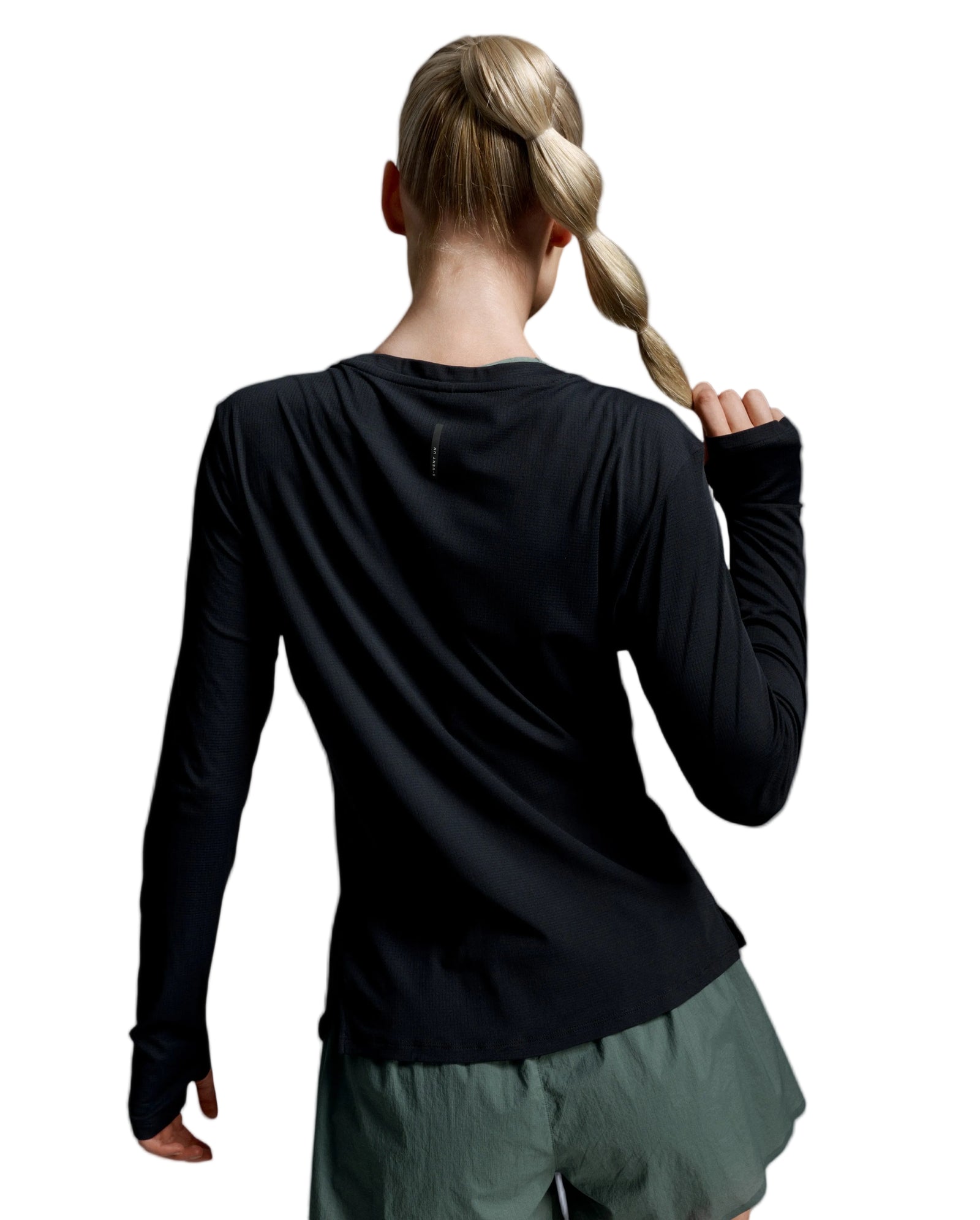 A woman shown from behind wearing a black long-sleeve athletic top and olive green shorts against a light gray studio background.