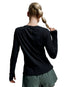 A woman shown from behind wearing a black long-sleeve athletic top and olive green shorts against a light gray studio background.