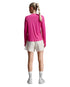 A woman shown from the back wearing a bright pink long-sleeve athletic top, off-white athletic shorts, white socks, and white sneakers against a light gray studio background.