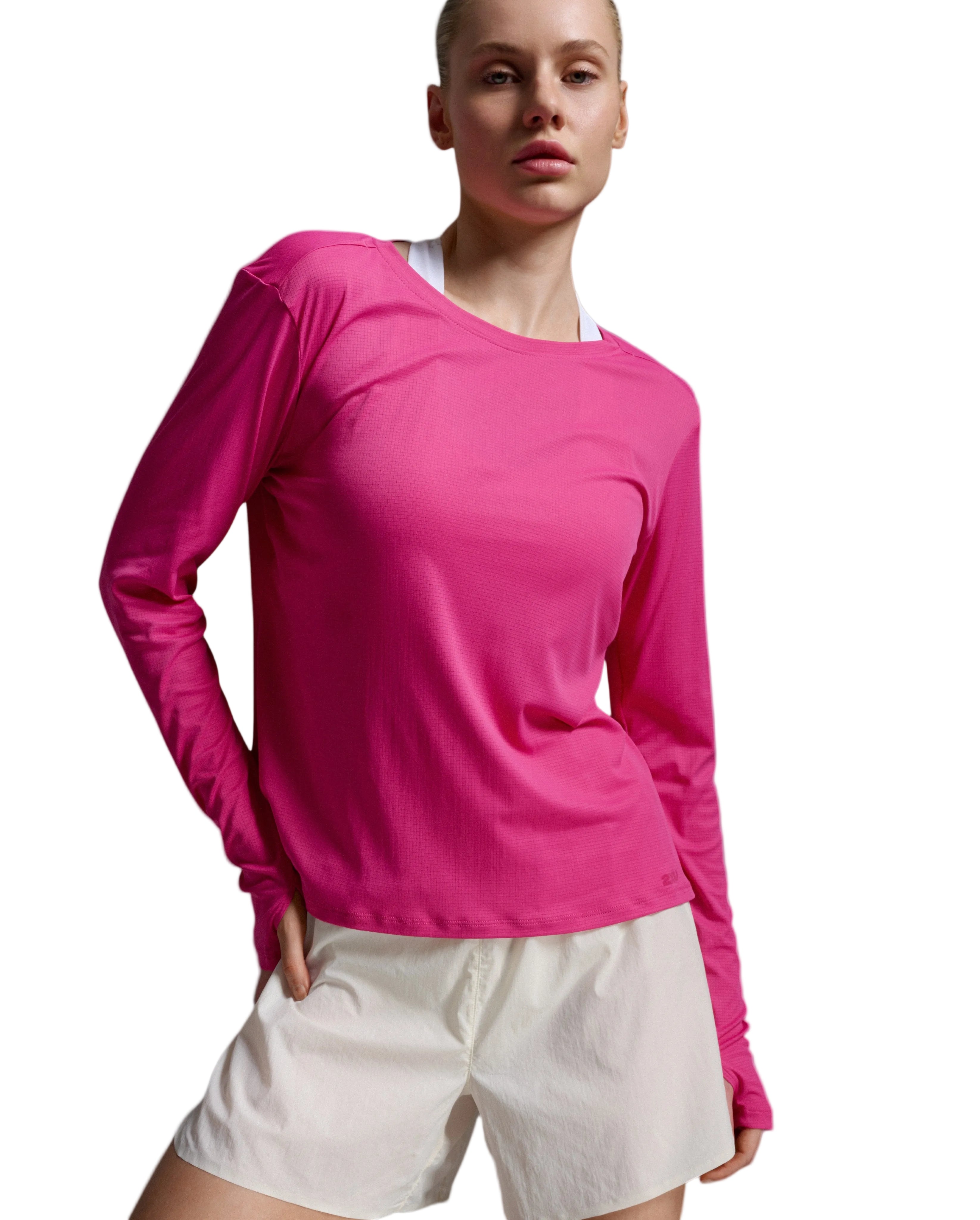 A model wearing a vibrant pink long-sleeve crewneck athletic top and off-white shorts, photographed against a neutral gray studio background.