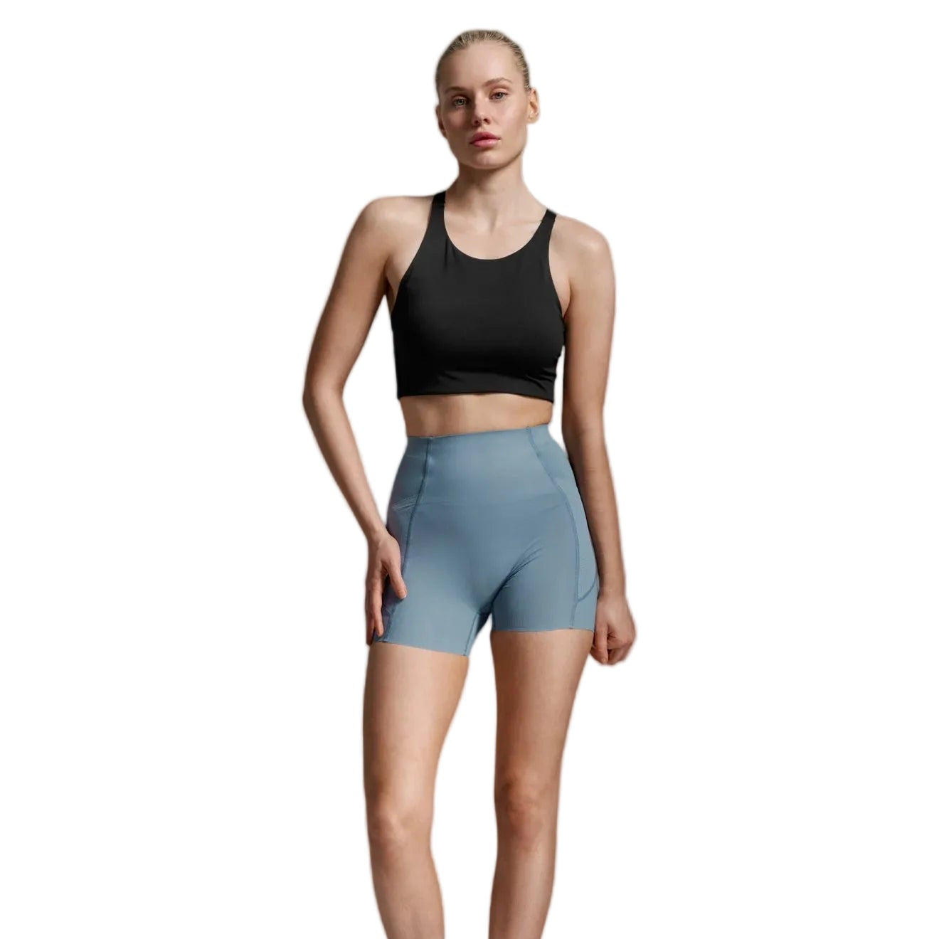 A woman modeling a black sports bra and light blue high-waisted athletic shorts against a light gray studio background.