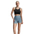 A woman modeling a black sports bra and light blue high-waisted athletic shorts against a light gray studio background.