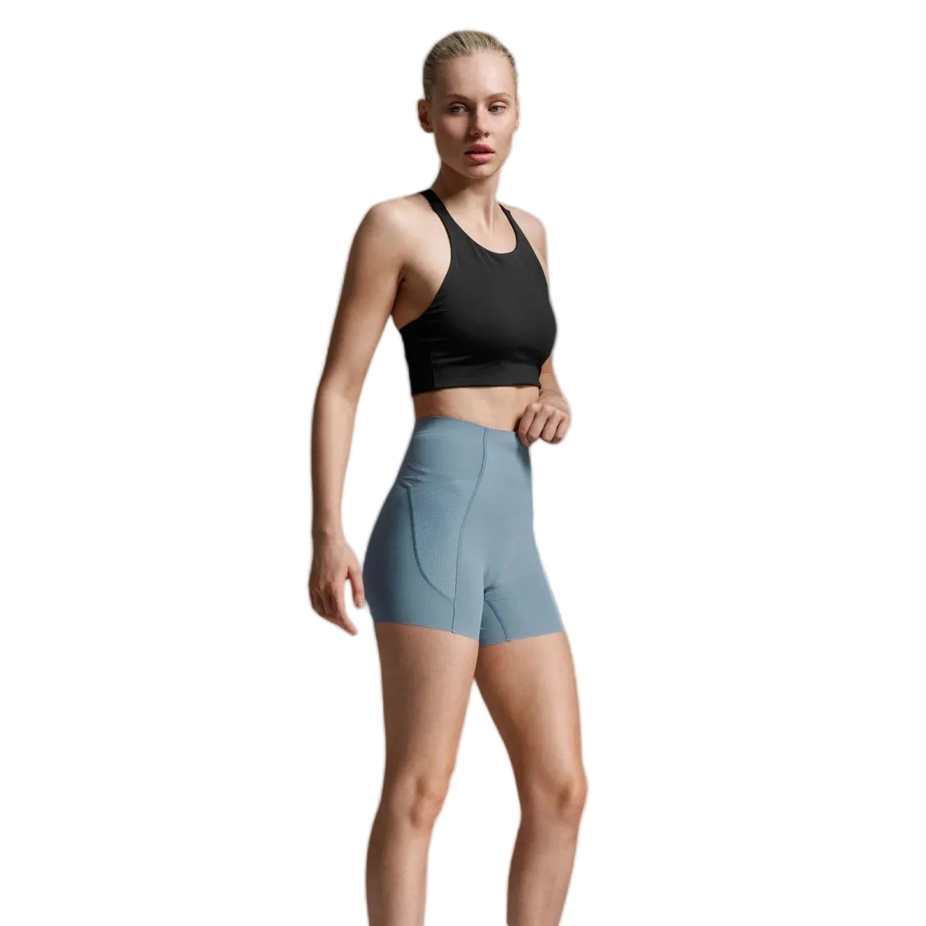 A woman modeling a black sports bra and light blue high-waisted athletic shorts against a light gray studio background.