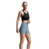 A woman modeling a black sports bra and light blue high-waisted athletic shorts against a light gray studio background.