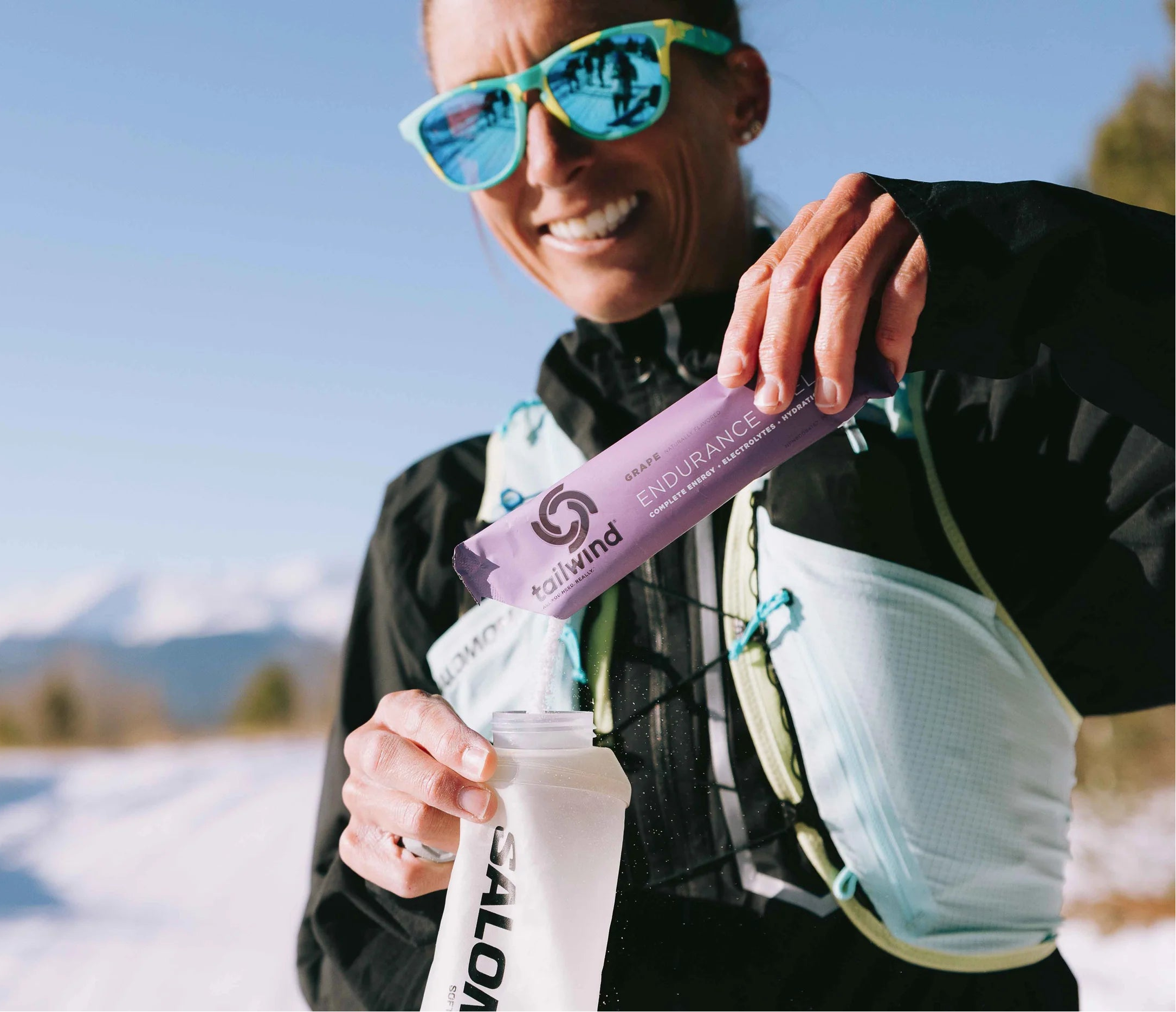 Person running outdoors with a water bottle and hydration system, mountainous background